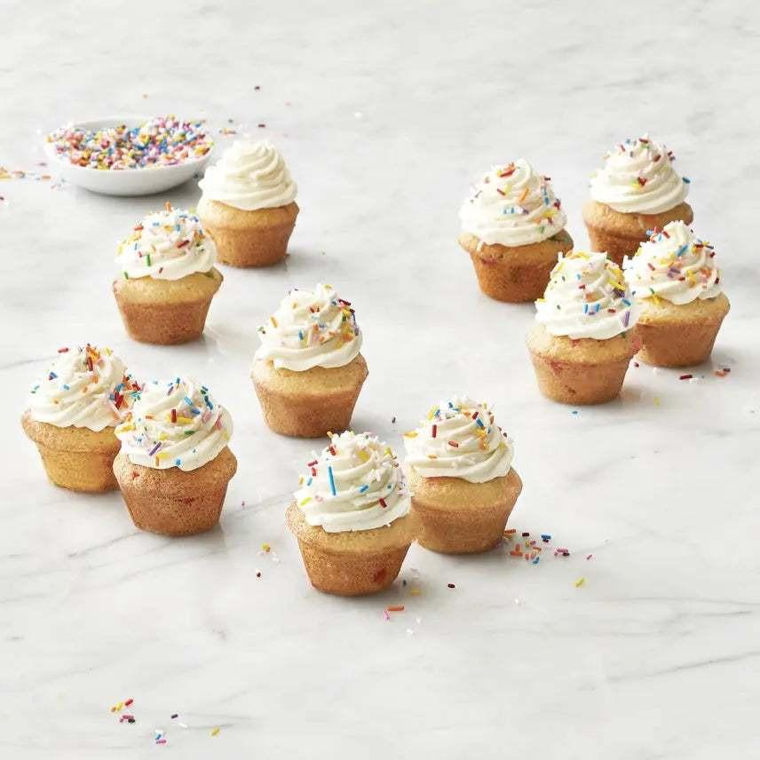 Mini muffins with white frosting and colorful confetti sprinkles on marble surface, made using a moule à 24 mini muffins confettis Trudeau silicone mold